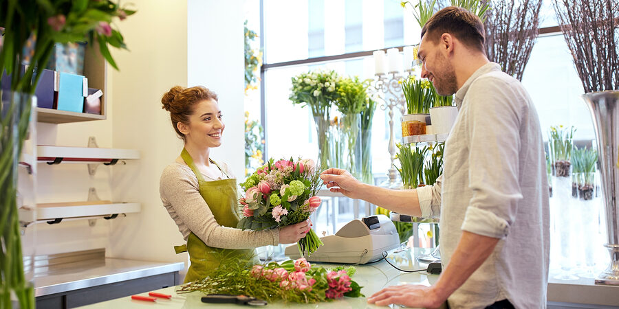 people, shopping, sale, floristry and consumerism concept - happy smiling florist woman making bouquet for and man or customer at flower shop