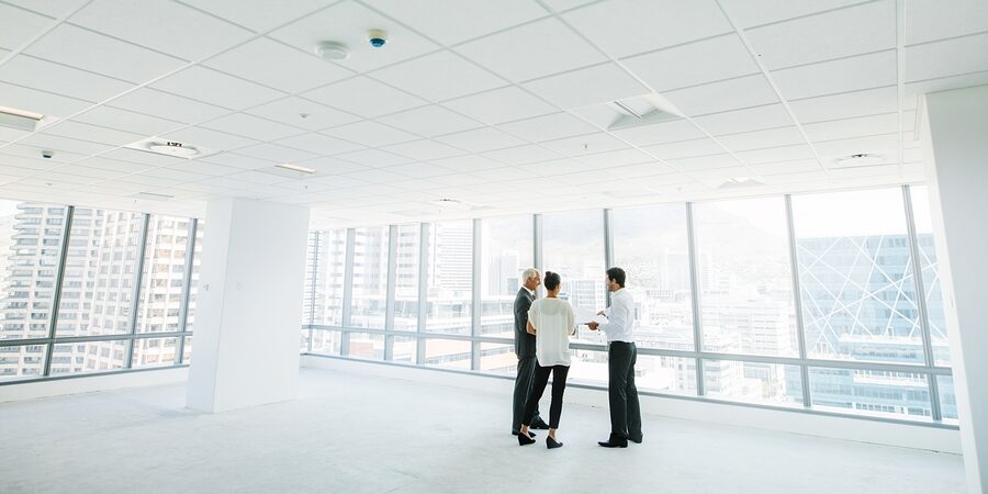 Wide angle shot of real estate agent with potential clients inside an empty office space. Estate broker showing new office space to business people.