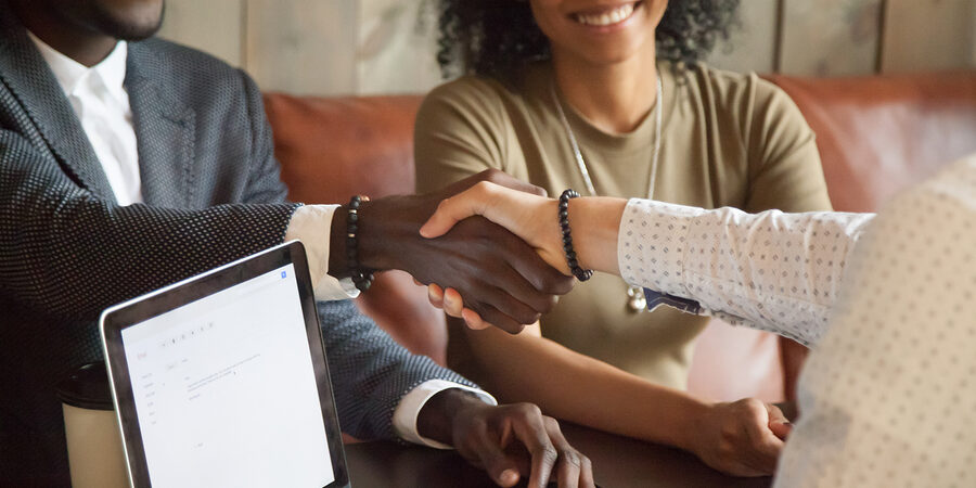 Happy young african american couple making deal handshaking caucasian insurance broker in cafe, black satisfied customer and realtor or sales person shaking hands at meeting in office with laptop