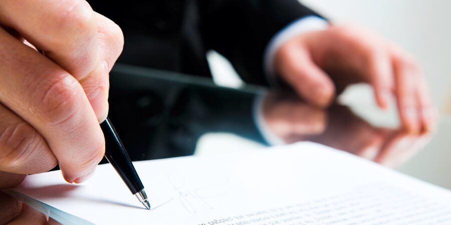 Closeup of business ladys hand with pen signing a contract on the background of her other hand touching the table